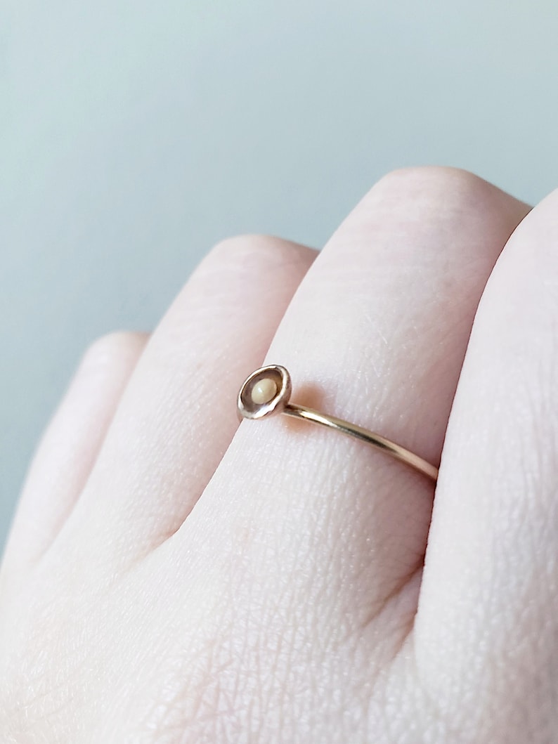 May include: A delicate gold ring with a small, round, cream-colored stone set in a simple, circular design.