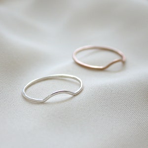Puede incluir: Dos anillos simples de plata y oro con un diseño curvo y abierto. Los anillos están sobre un fondo de tela blanca.