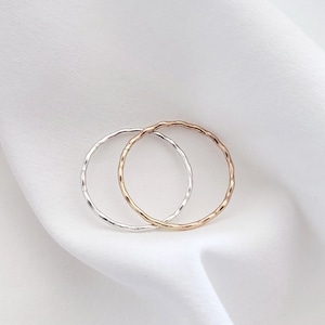 May include: Two thin, silver and rose gold rings with a textured, hammered finish. The rings are stacked on top of each other.