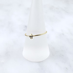 Pode incluir: Um anel de ouro com um pequeno design de caveira. O anel est&aacute; em um expositor branco.