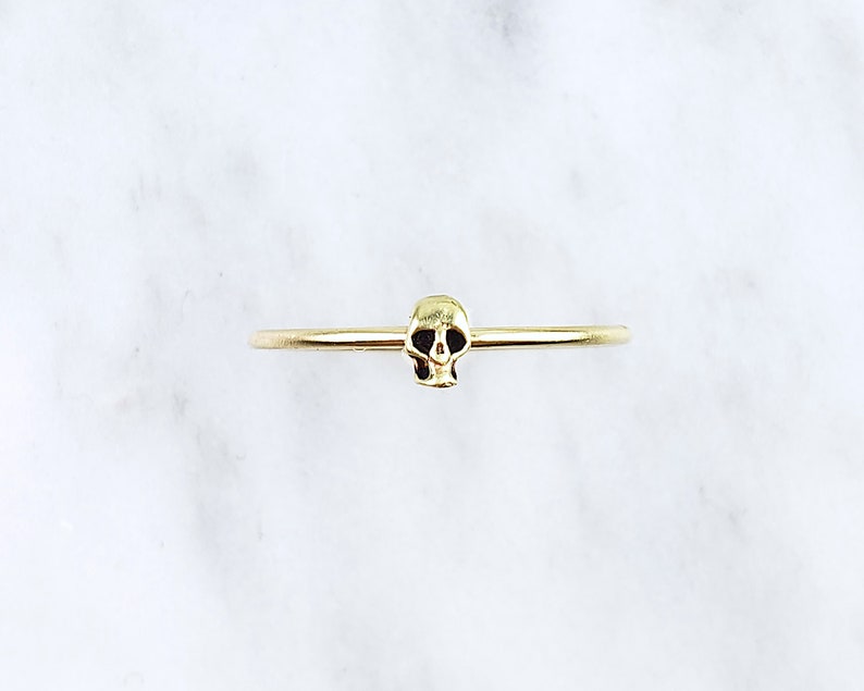 Pode incluir: Um anel de ouro com um pequeno design de caveira.