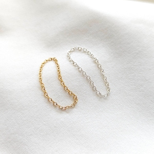 May include: Two delicate chain rings, one gold and one silver, on a white background.