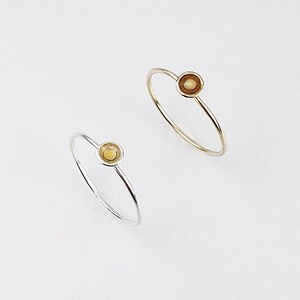 May include: Two simple rings with a small, round, yellow-gold colored stone set in the center of each ring. The ring on the left is silver and the ring on the right is gold.
