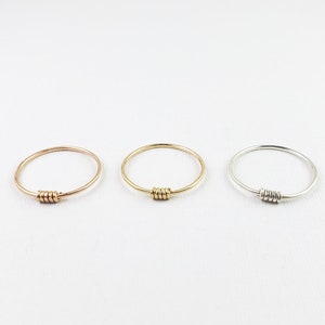 May include: Three simple rings with a twisted wire detail. The rings are in gold, rose gold, and silver.