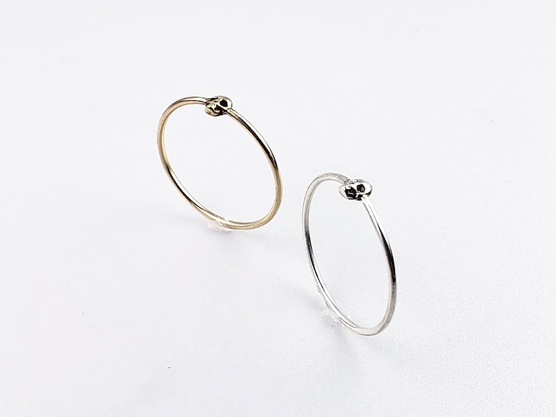 Puede incluir: Dos anillos simples con un dise&ntilde;o de calavera. Un anillo es de oro y el otro es de plata.