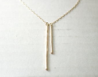 May include: A gold necklace with two thin, vertical bars hanging from the chain.