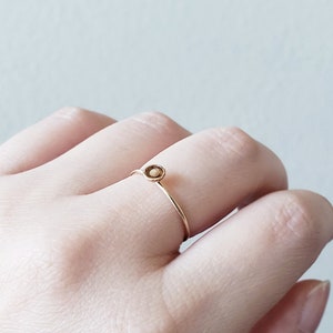 May include: A delicate gold ring with a small, round, light brown stone set in the center.