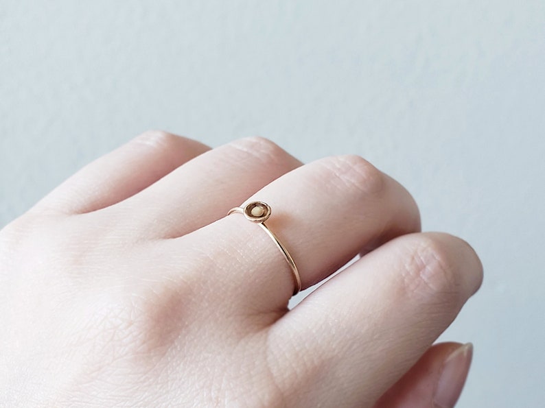 May include: A delicate gold ring with a small, round, light brown stone set in the center.