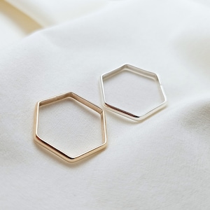 May include: Two hexagon-shaped rings, one gold and one silver, on a white fabric background.
