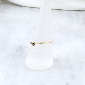 Pode incluir: Um anel de ouro com um pequeno design de caveira. O anel &eacute; exibido em um suporte c&ocirc;nico branco.