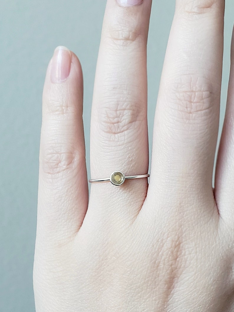 May include: A delicate silver ring with a small, round, light green gemstone.