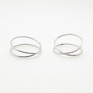 May include: Two silver-colored rings with an overlapping design. Each ring features two connected, circular bands that intersect. The rings are displayed on a white background, highlighting their minimalist and modern aesthetic. These rings are suitable for everyday wear.