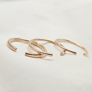 May include: Three gold-toned metal rings, each with a slightly different shape and size, are arranged on a white surface.