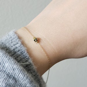 Pode incluir: Um delicado bracelete de corrente dourada com um pequeno fecho de caveira preta.