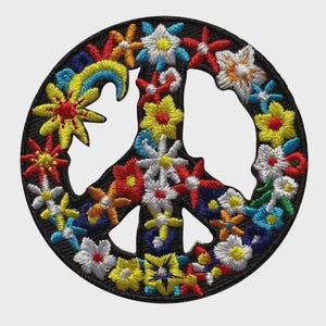 May include: A circular embroidered patch featuring a peace sign symbol. The design is filled with colorful stitched flowers in shades of yellow, red, white, orange, and blue, set against a black background with a thick black border.