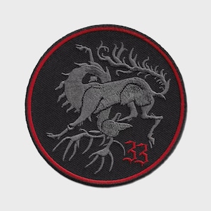 May include: A circular embroidered patch featuring a black background with a red border. The design depicts a grey mythical creature with antlers and a long tail, positioned above the red embroidered number 33 in a gothic-style font.