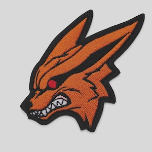 May include: An embroidered patch featuring the stylized head of a fox with orange fur, black outlines, and a red eye. The fox has a snarling expression with visible white teeth and pointed ears, finished with a thick black border around the edges.