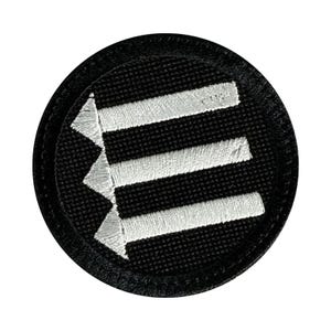 May include: A circular embroidered patch featuring a black background with three horizontal white arrows pointing to the left. The design is enclosed within a thick black stitched border, creating a clean and high-contrast graphic emblem.