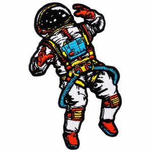 May include: An embroidered patch featuring an astronaut in a white spacesuit with a black helmet. The suit includes bright blue, yellow, and red accents, with a blue hose extending from the chest pack. The design is outlined in thick black thread.