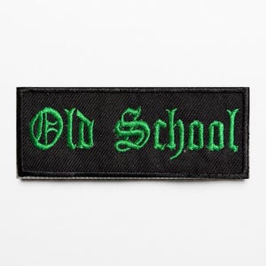May include: A rectangular embroidered patch with a black background and a black border. The text Old School is stitched in a bright green, gothic-style font across the center of the patch, featuring a textured thread finish throughout.