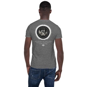 May include: A heather gray short-sleeve t-shirt featuring a circular graphic on the back. The design includes a medical cross-section image, the letters CT, and the text Computed Tomography, LIVES AT LATER, with a small icon below the text.