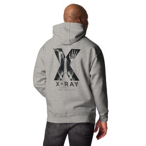 May include: A heather gray hooded sweatshirt featuring a large black letter X on the back. Inside the X are white skeletal X-ray images of a rib cage, hand, and pelvis. Below the graphic, the text reads X-RAY and SEE BEYOND in black lettering.
