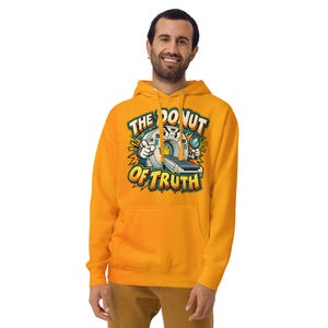 May include: A bright yellow hooded sweatshirt featuring a graphic print of a cartoon medical scanner with arms and a magnifying glass. The text above and below the illustration reads THE DONUT OF TRUTH in bold, colorful, block-style lettering.