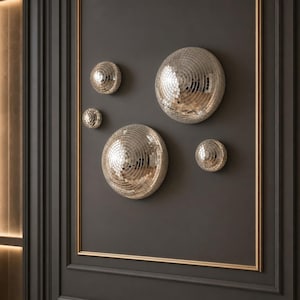 May include: A collection of four circular, silver-toned disco ball wall decorations of varying sizes. Each piece is constructed from numerous small, reflective square mirror tiles arranged in a spherical, convex shape, creating a faceted surface.