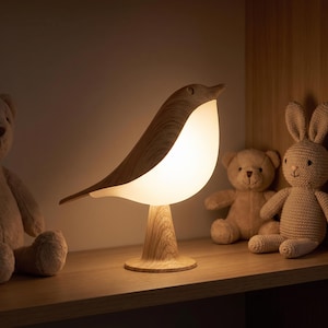 May include: A bird-shaped table lamp featuring a wood-grain textured base and back, with a smooth, glowing white light-diffusing body. The lamp stands upright on a circular base, emitting a soft, warm illumination from its central section.