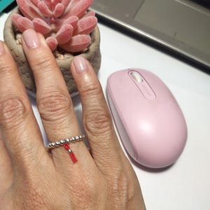 May include: A silver beaded ring with a red tassel charm. The ring is worn on a person's finger.