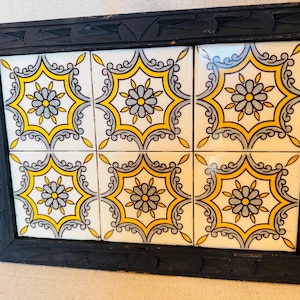 May include: A rectangular serving tray featuring a black carved wooden frame with integrated handles. The centre is inlaid with six square ceramic tiles, each displaying a repeating yellow, grey, and white floral geometric pattern.