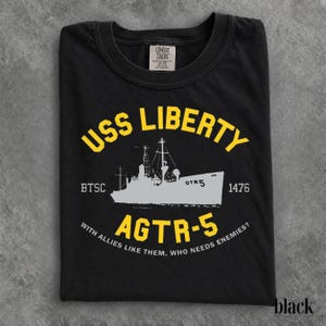 以下が含まれることがあります： USSリバティ号の白いグラフィックがプリントされた黒いTシャツ。テキストには「USS LIBERTY」「AGTR-5」「BTSC 1476」「WITH ALLIES LIKE THEM, WHO NEEDS ENEMIES?」と記されています。暗い色の生地に黄色と白の文字がデザインされています。