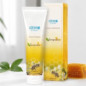 Puede incluir: Un tubo de pasta de dientes Atomy blanco y amarillo junto a su caja rectangular a juego. Ambos artículos presentan el texto Atomy Toothpaste y Propolis, junto con gráficos de una abeja y un patrón de panal. El peso neto es de 200g.