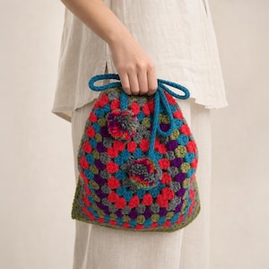 Handmade, crocheted, multi colored, granny square bag with red lining, peacock bow, two pom poms and red lining. Back is solid red crochet.