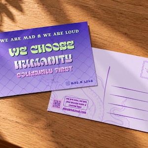 May include: A rectangular postcard with a purple background featuring a chain-link fence pattern and the text WE ARE MAD & WE ARE LOUD, WE CHOOSE HUMANITY, SOLIDARITY FIRST. The reverse side is light purple with lines for writing and a QR code.