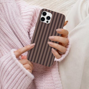 May include: A smartphone case featuring a vertical striped pattern in alternating shades of dark brown and light brown. The case has a rectangular cutout at the top left corner for the camera lenses and flash, maintaining a clean and simple design.