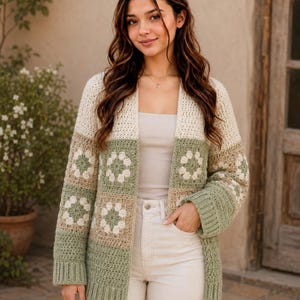 May include: A long-sleeve open-front cardigan featuring a crochet granny square pattern in shades of sage green, cream, and tan. The garment has a solid cream-coloured upper section, ribbed cuffs, and a ribbed hem, constructed with a textured yarn.
