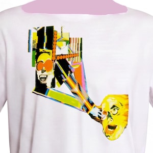 May include: A white t-shirt featuring a colourful graphic print of two stylised faces with distorted features, vibrant orange, yellow, and green hues, and geometric patterns that create a fragmented, collage-like visual effect across the chest area.