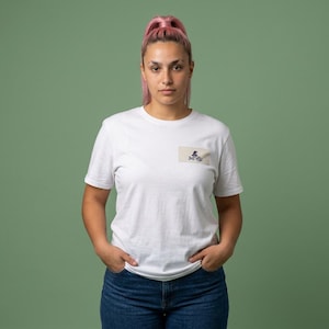 May include: A white short-sleeved t-shirt featuring a small rectangular patch on the left chest. The patch is light beige and displays a dark purple graphic of a witch hat above the text "Spooky" in a stylized, dark purple cursive font.