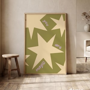 Puede incluir: Un cuadro rectangular con marco que presenta un patrón repetitivo de estrellas grandes de color crema claro sobre un fondo verde oliva. El texto 'you are magic' está impreso en una fuente sans-serif redondeada de color violeta claro.