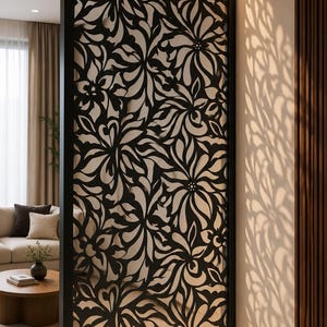 May include: A tall, rectangular room divider featuring a black metal frame and an intricate, laser-cut floral pattern. The screen is backlit, casting detailed, elongated shadows of the flower design onto the adjacent wall surface.
