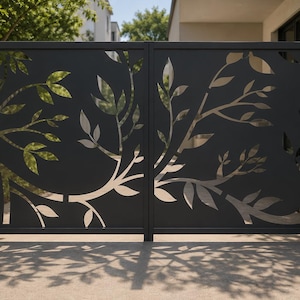 May include: A double gate made of matte black metal featuring a laser-cut design of branches and leaves. The cutouts reveal the light behind the gate, creating a silhouette effect. The gate is framed by two light-colored stone pillars with lights.