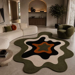 May include: An irregular, organic-shaped area rug featuring a layered, wavy pattern in concentric rings of olive green, cream, black, and burnt orange. The rug has a soft, textured pile and a distinct, non-symmetrical silhouette with rounded edges.