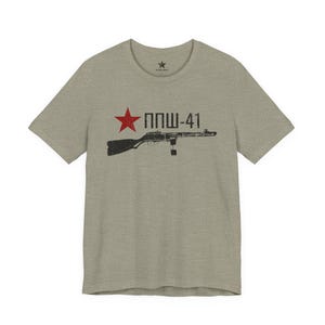 May include: A heathered light olive green short-sleeve t-shirt featuring a graphic print on the chest. The design includes a red five-pointed star, the black text "ППШ-41", and a black silhouette of a submachine gun with a distressed texture.