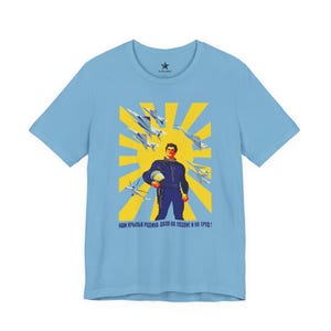May include: A light blue short-sleeve t-shirt featuring a graphic print of a pilot in a dark blue flight suit holding a helmet, surrounded by fighter jets against a yellow sunburst background with the text "НАМ КРЫЛЬЯ РОДИНА ДАЛА НА ПОДВИГ И НА ТРУД!"