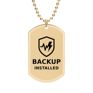 Op de afbeelding: Een goudkleurige metalen dog tag hanger aan een bijpassende kralenketting. De hanger is voorzien van een zwarte gravure van een schild met een bliksemschicht en een hartslaglijn, met de zwarte tekst BACKUP INSTALLED onder het schild.