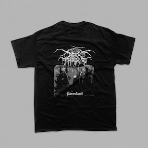 May include: A black short-sleeved t-shirt featuring a white graphic print. The design includes the text Darkthrone in a stylised font above a rectangular image of a dark forest scene with a moon, and the word Panzerfaust printed below the image.