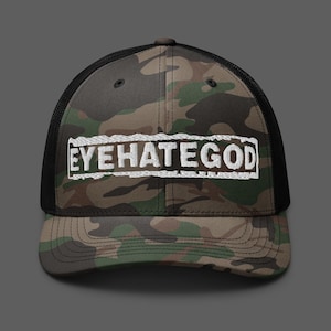 Puede incluir: Una gorra tipo trucker con estampado de camuflaje, parte trasera de malla negra y panel frontal estructurado. El frente presenta un parche rectangular bordado en blanco con el texto EYEHATEGOD en letras mayúsculas blancas y negritas.