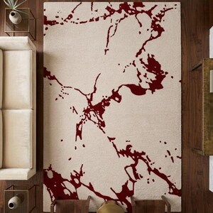 Puede incluir: Una alfombra rectangular con una base de color crema y un patr&oacute;n abstracto audaz en rojo oscuro que se asemeja a vetas de m&aacute;rmol org&aacute;nicas y fluidas o salpicaduras de tinta extendidas por toda la superficie del revestimiento.