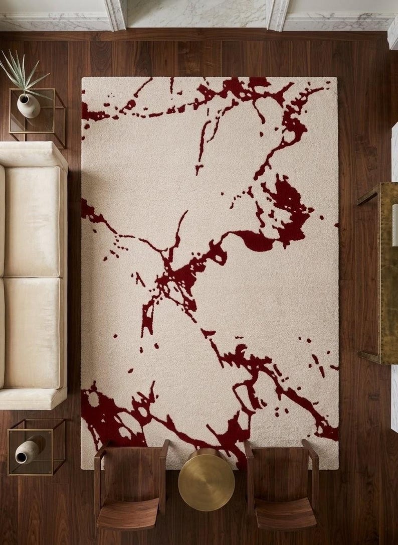 Puede incluir: Una alfombra rectangular con una base de color crema y un patr&oacute;n abstracto audaz en rojo oscuro que se asemeja a vetas de m&aacute;rmol org&aacute;nicas y fluidas o salpicaduras de tinta extendidas por toda la superficie del revestimiento.